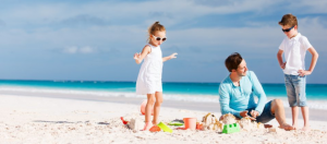 dad builds a sandcastle with son and daughter on beach