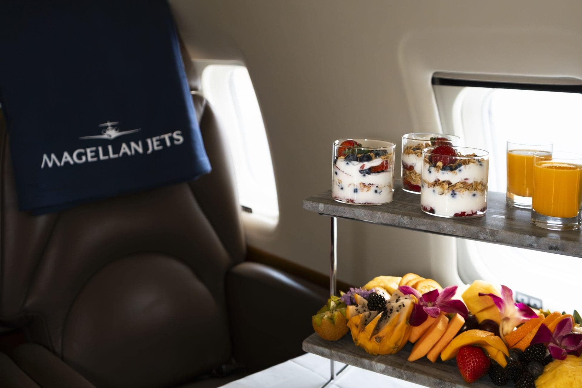 Close-up of a fresh fruit tray and cashmere blanket on a private jet seat, illustrating in-flight catering aboard a private jet
