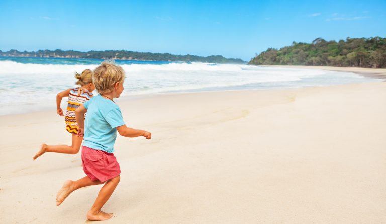 Happy barefoot kids have fun on beach walk. Run and jump by white sand along sea surf. Family travel lifestyle, outdoor sports activities and games. Summer vacation with children on tropical island