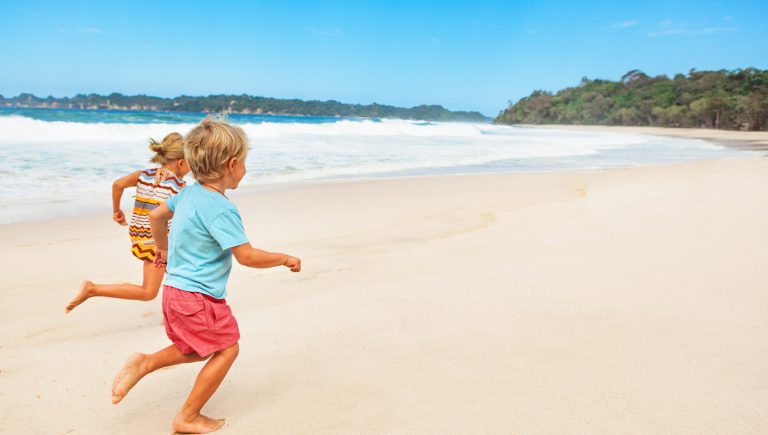 Happy barefoot kids have fun on beach walk. Run and jump by white sand along sea surf. Family travel lifestyle, outdoor sports activities and games. Summer vacation with children on tropical island