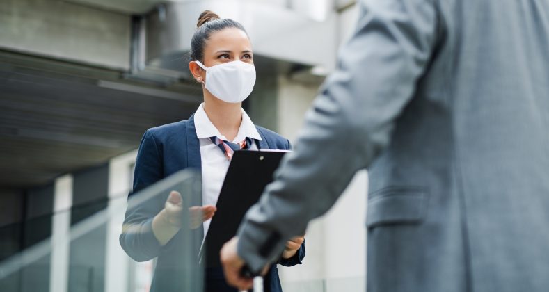 Attractive flight attendant talking to unrecognizable businessman on airport, wearing face masks.