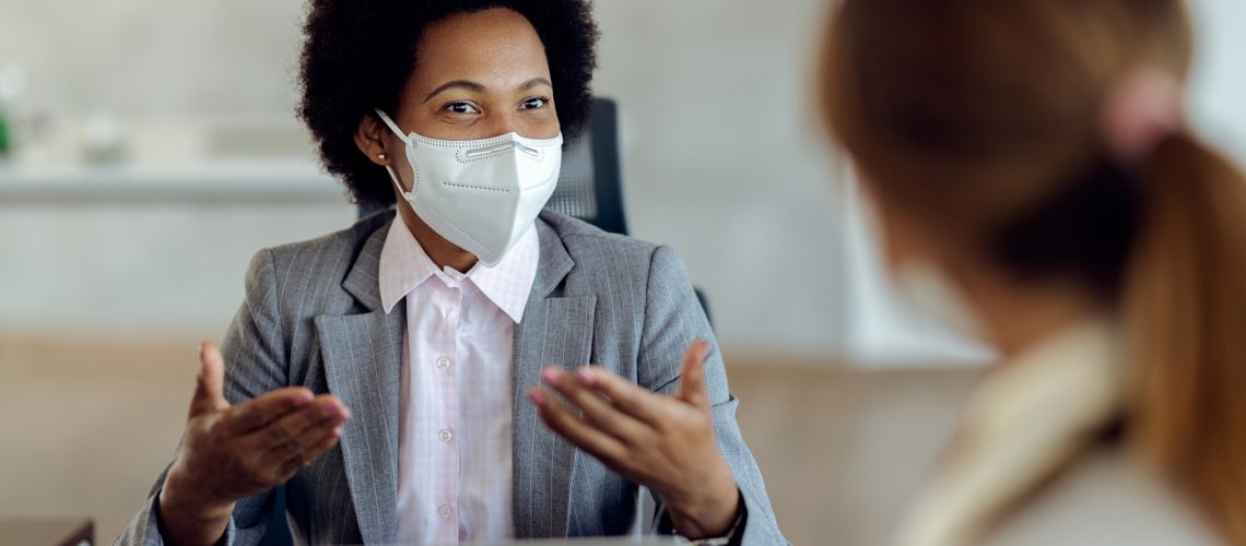 African American bank manager with protective face mask communicating with her client during a meeting in the office.