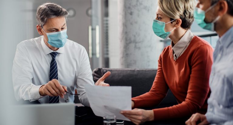 Insurance agent talking to a couple while having a meeting in the office during coronavirus pandemic.
