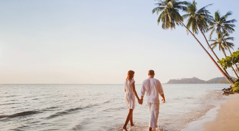 romantic young couple walking together on beautiful exotic tropical beach at sunset