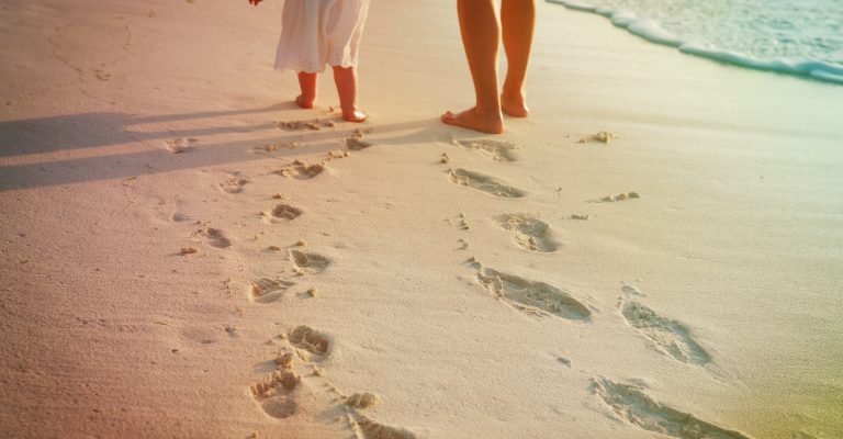 mother and little daughter walking on beach leaving footprint in sand