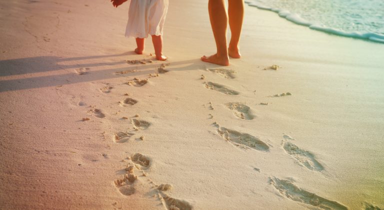 mother and little daughter walking on beach leaving footprint in sand
